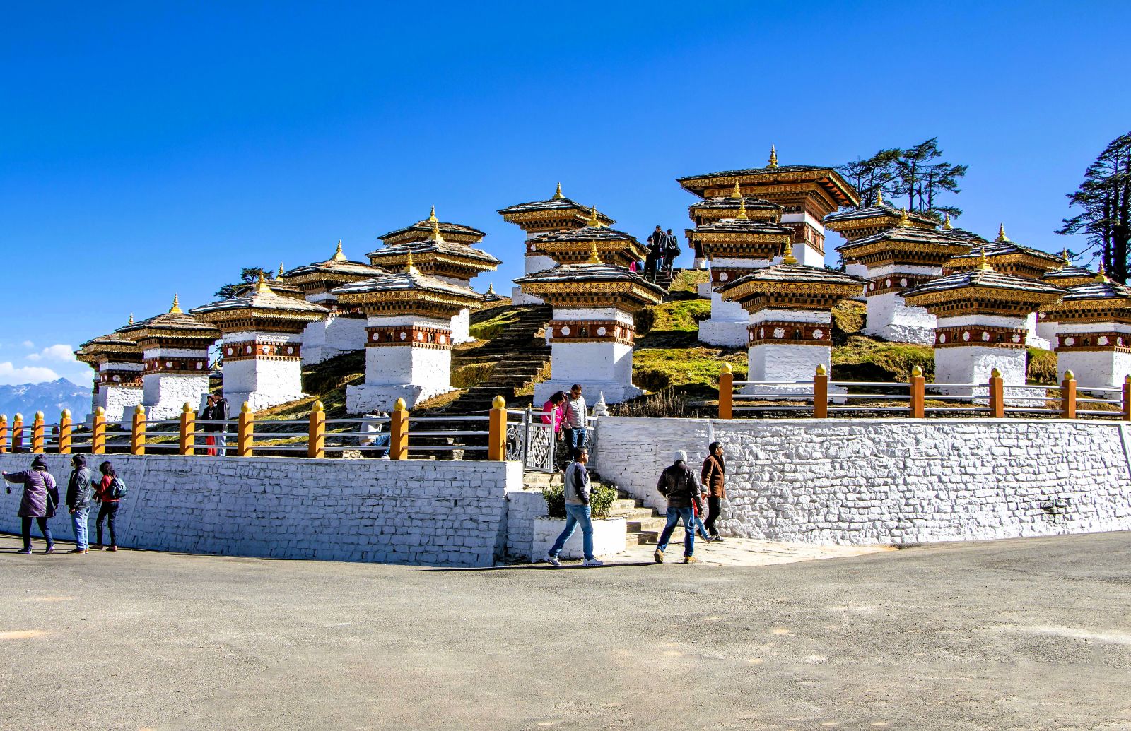 Scenic view of Dochula Pass featuring the 108 Druk Wangyal Chortens, colorful prayer flags, and snow-capped Himalayan peaks rising above misty valleys at sunrise.