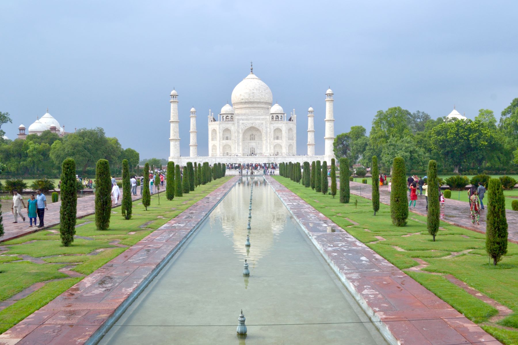 Front view of Taj Mahal showcasing its white marble façade, reflecting pool, symmetrical Mughal gardens, and clear blue sky.